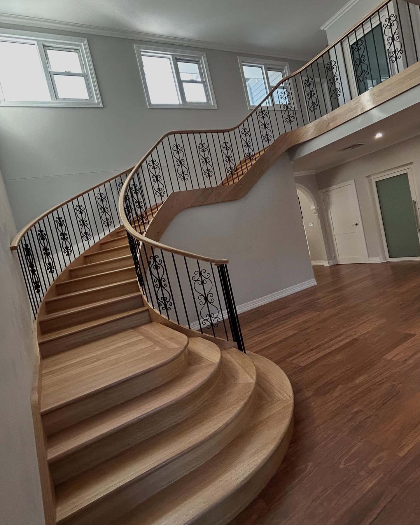 1-home-about-section1 Curved timber staircase with wrought iron balustrade rising to a landing