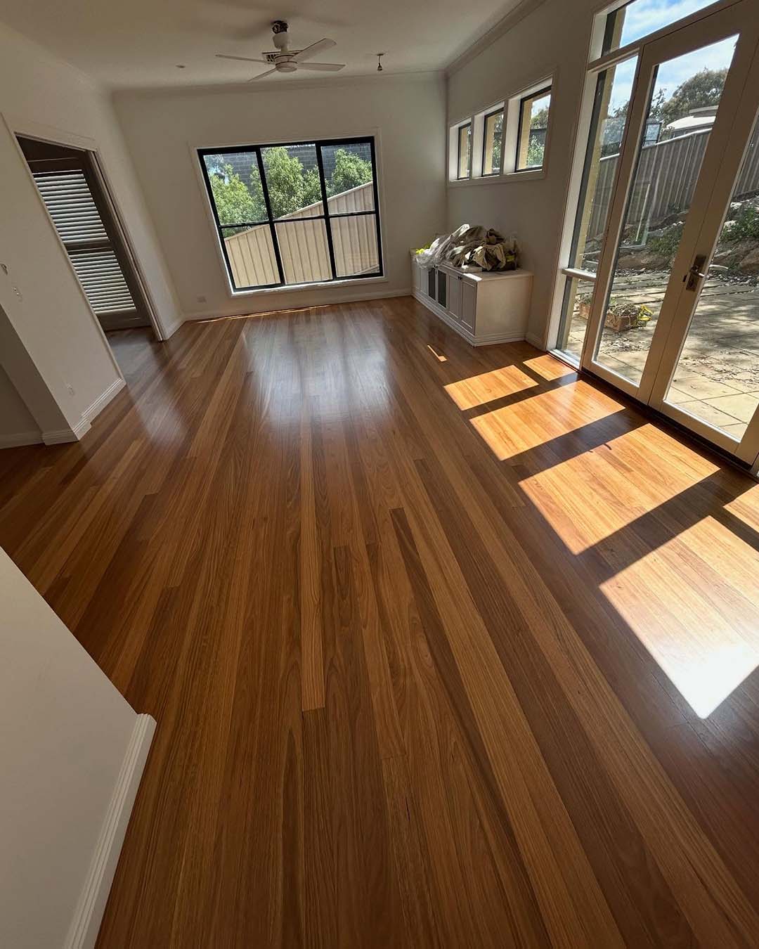 Glossy timber floor in a sunlit living room with glass doors