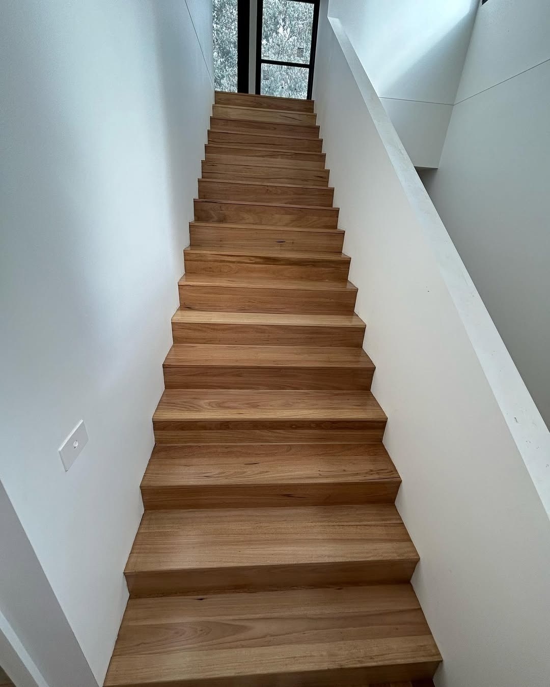Straight timber staircase between white walls, seen from below