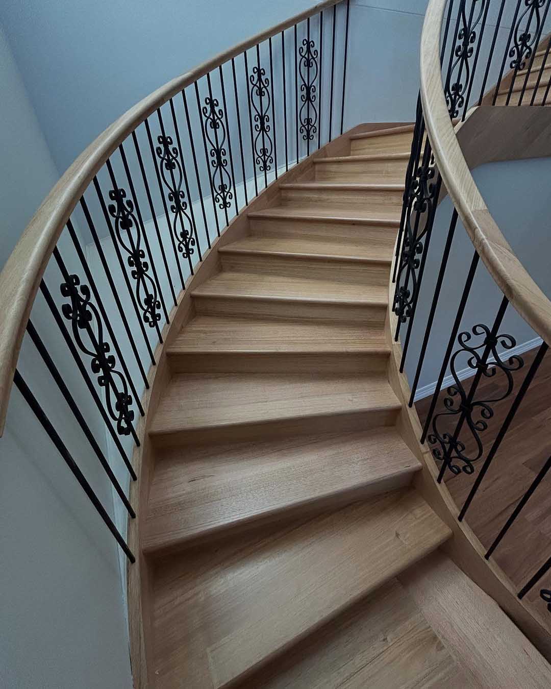 Curved timber staircase with wrought iron balustrades, looking up