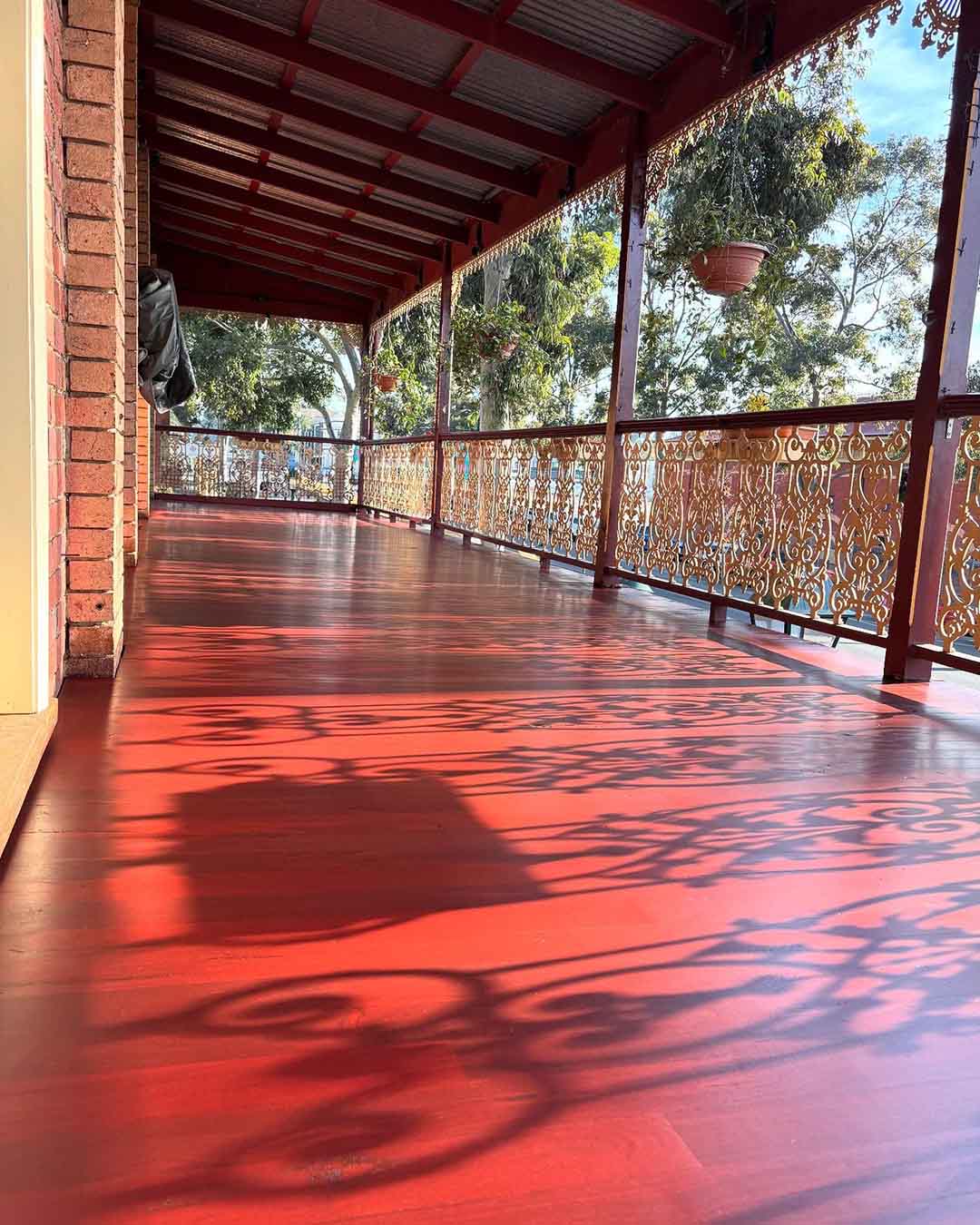 Red verandah floor with lacy shadows from the iron railing