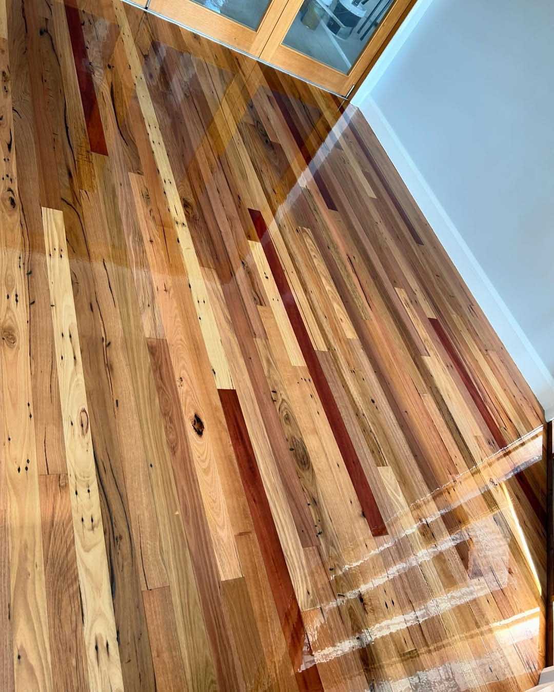 Glossy mixed-colour timber boards, including red-toned boards, seen from above