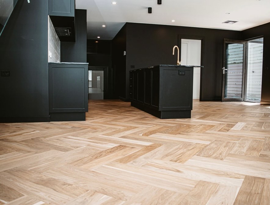 faq3 Light herringbone floor through an open-plan kitchen with black cabinets