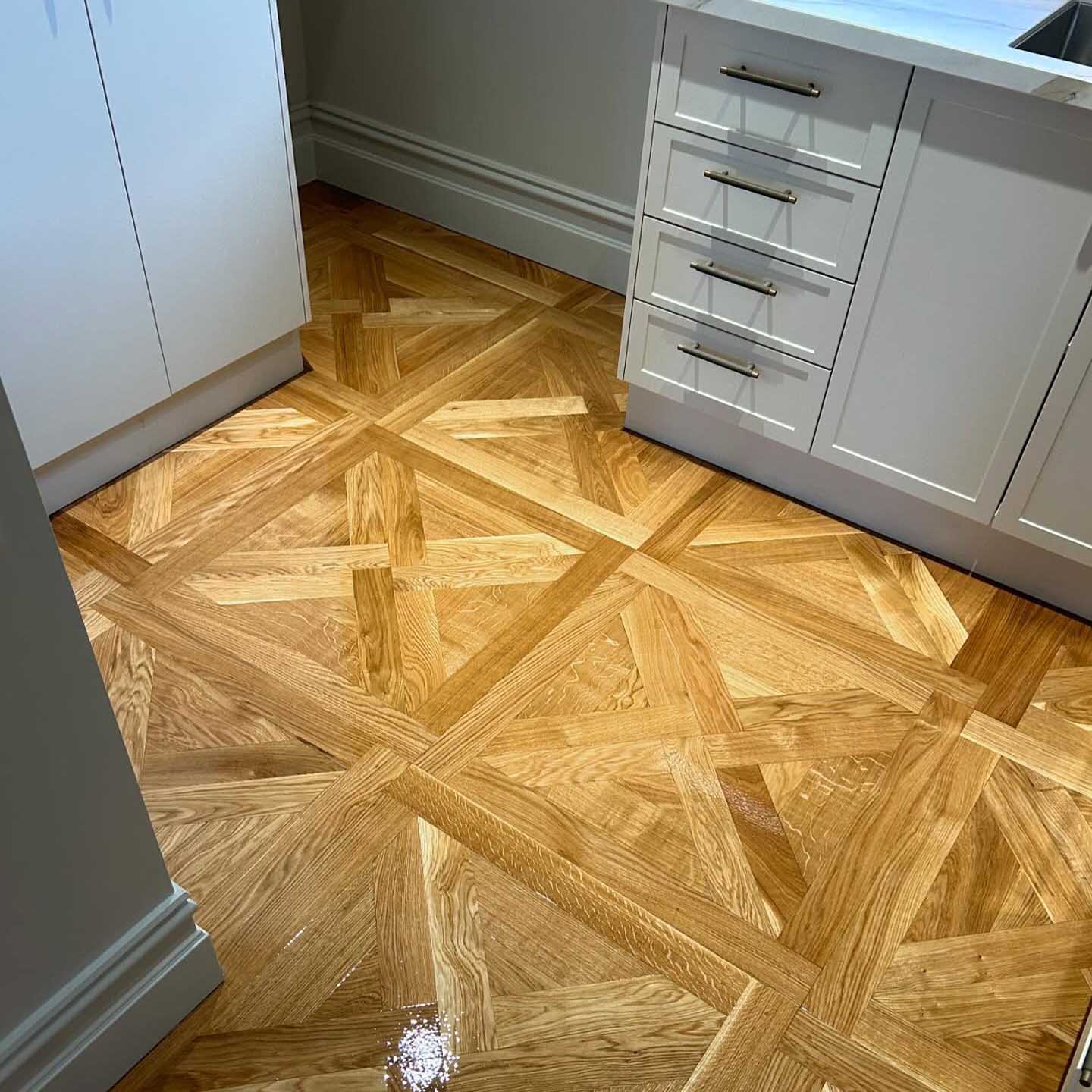 Glossy parquetry floor in a large lattice pattern between kitchen cabinets