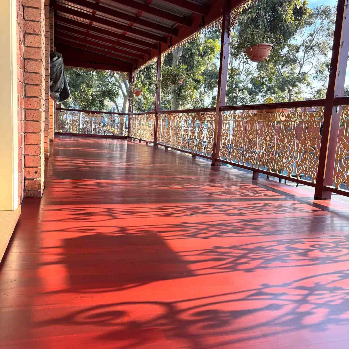 Glossy red timber verandah floor with shadows from the ornate railing