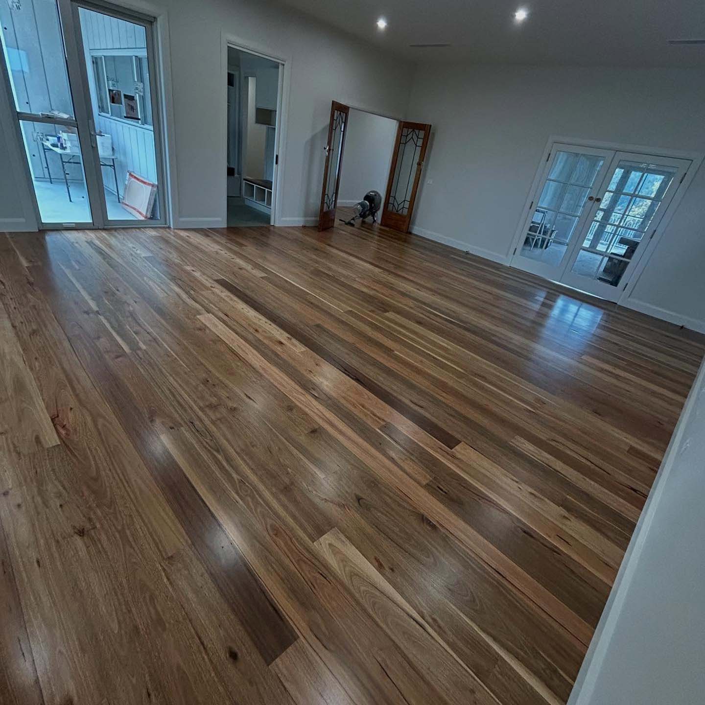 Glossy multi-toned timber strip floor in a large empty room with French doors
