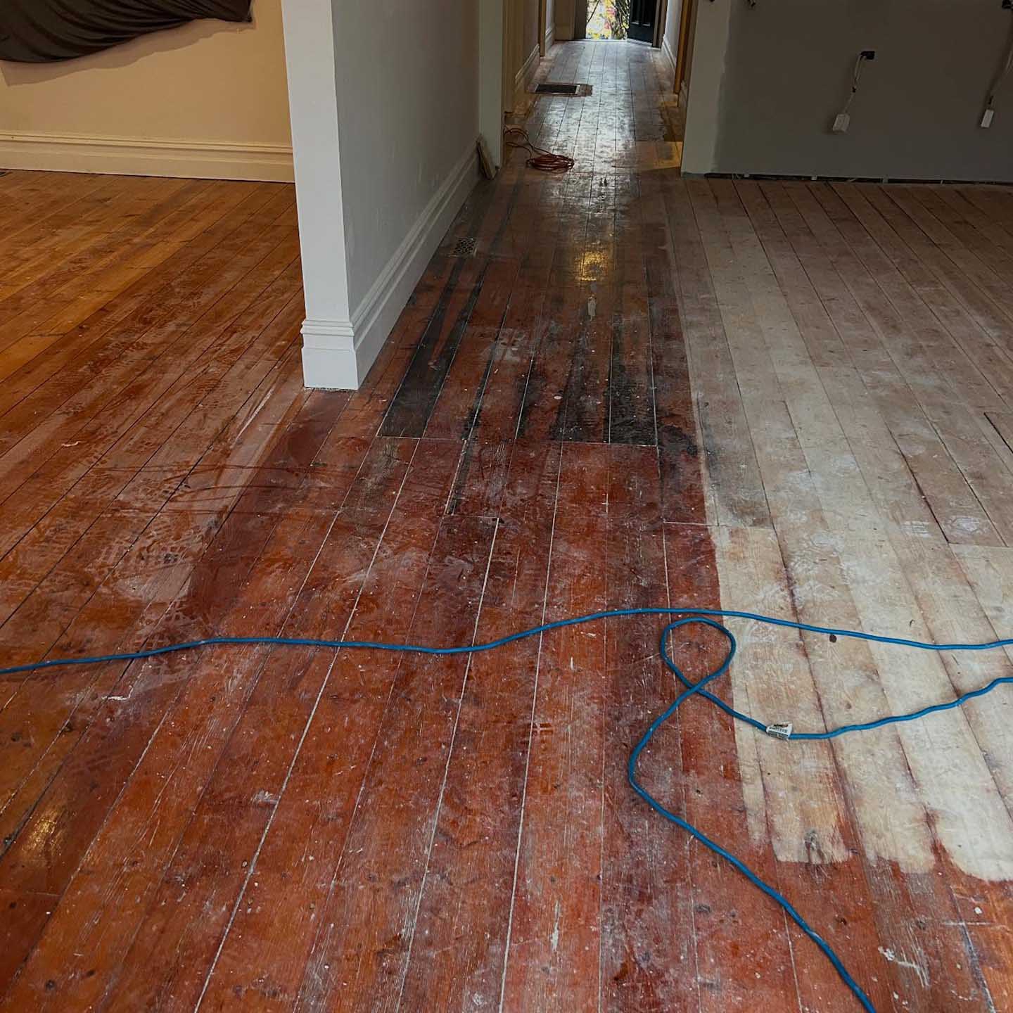 Hallway floorboards part-sanded, old dark finish next to bare timber