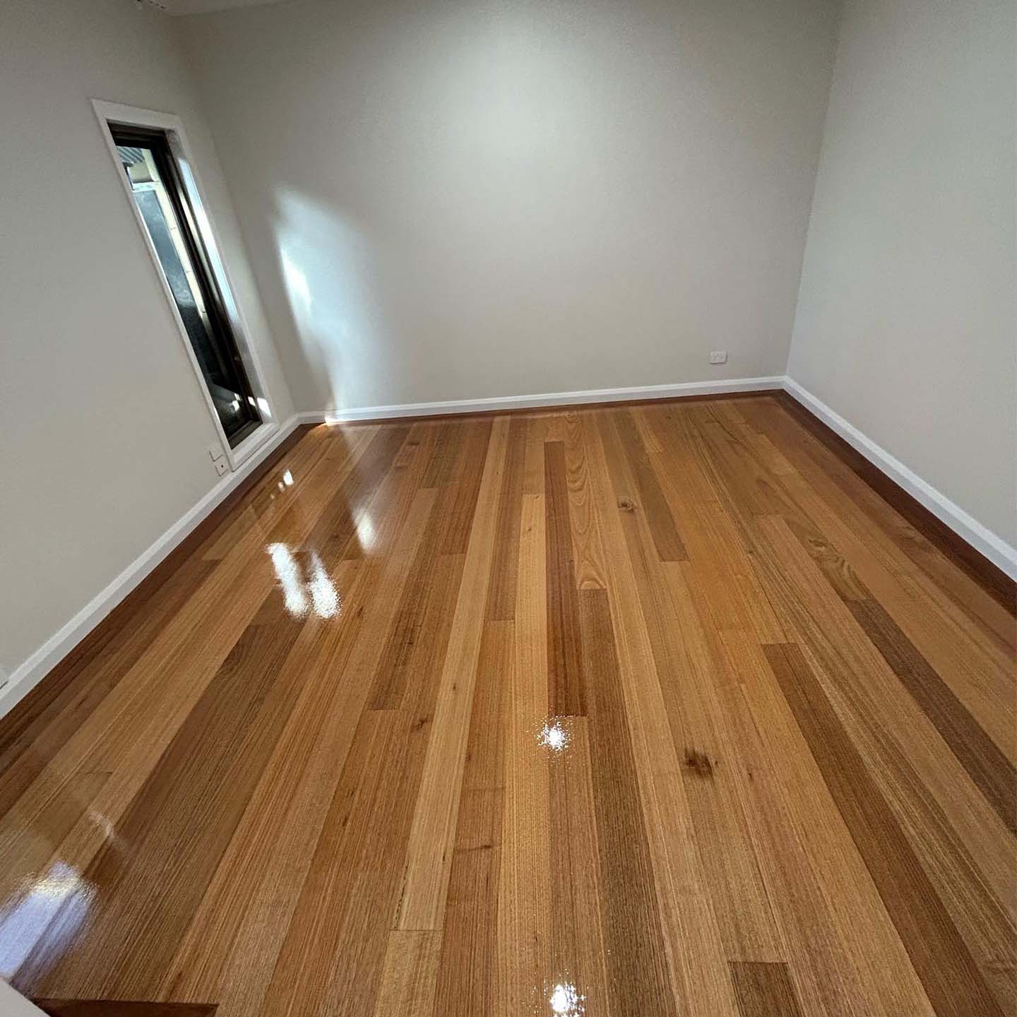Glossy timber strip floor in an empty bedroom with white walls