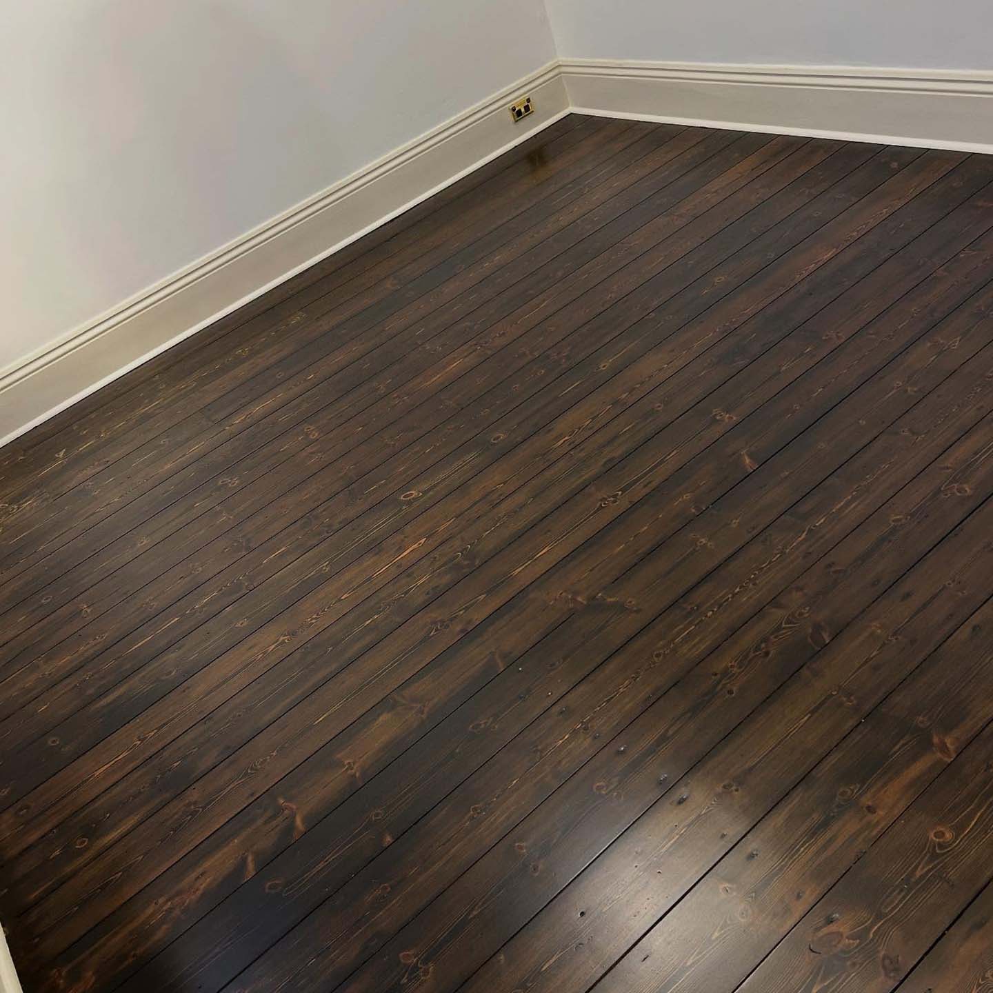 Dark stained timber floorboards in an empty room with white skirting